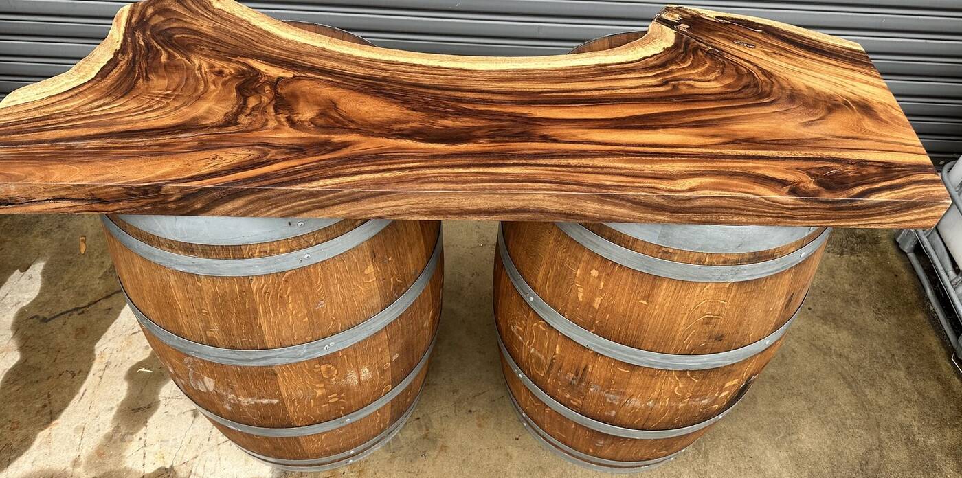 Two oak wine barrels topped with a live-edge timber slab forming a rustic bar